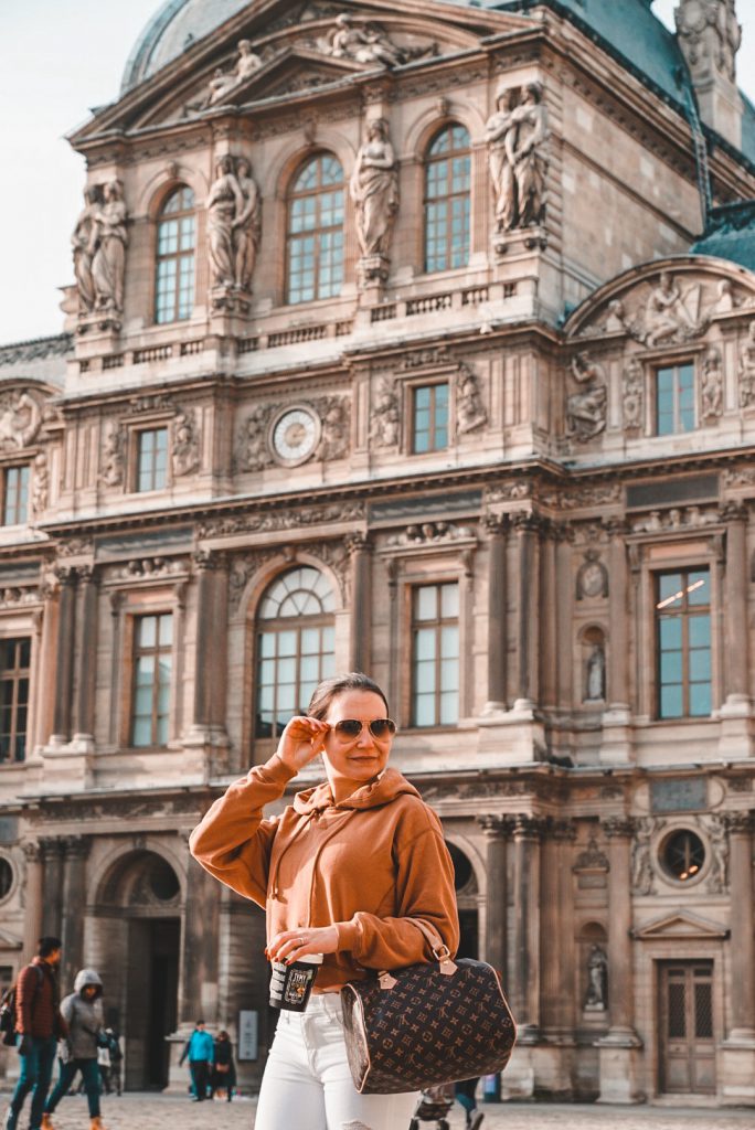 A girl standing in front of the Louvre museum in Paris.